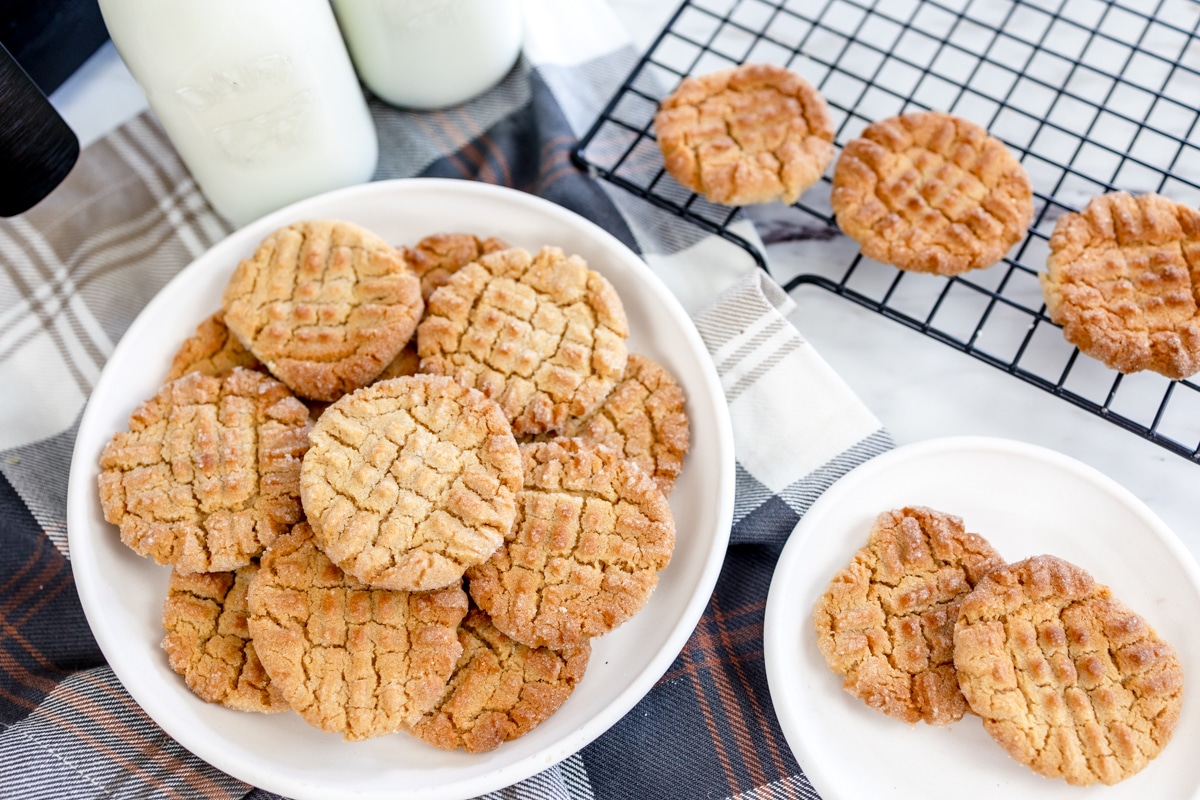 Top view of air fryer peanut butter cookies in a pile on a plate next to some glassed of milk.