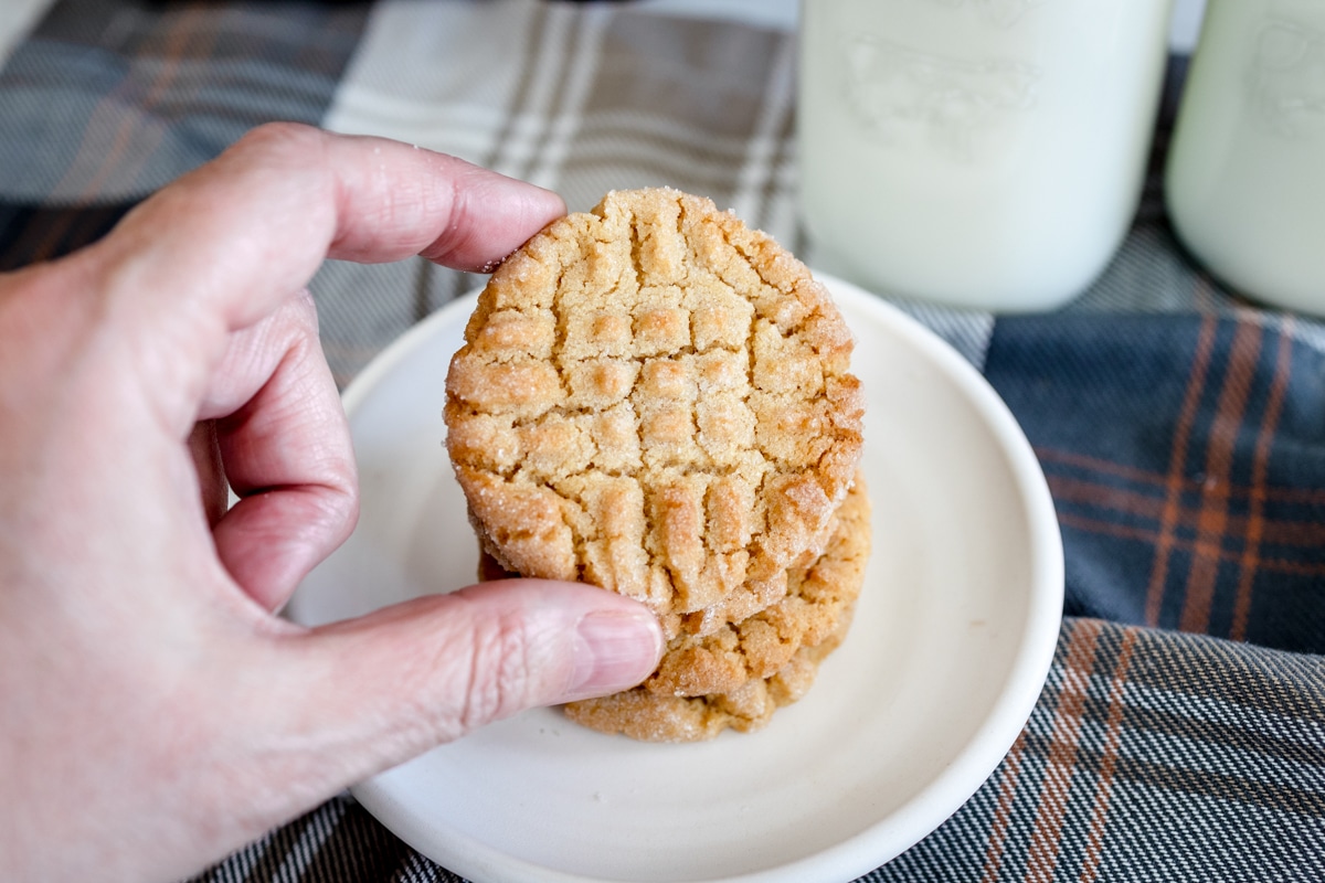 Top view close up of a peanut butter cookie being held in mid air on top of a plate by a hand.