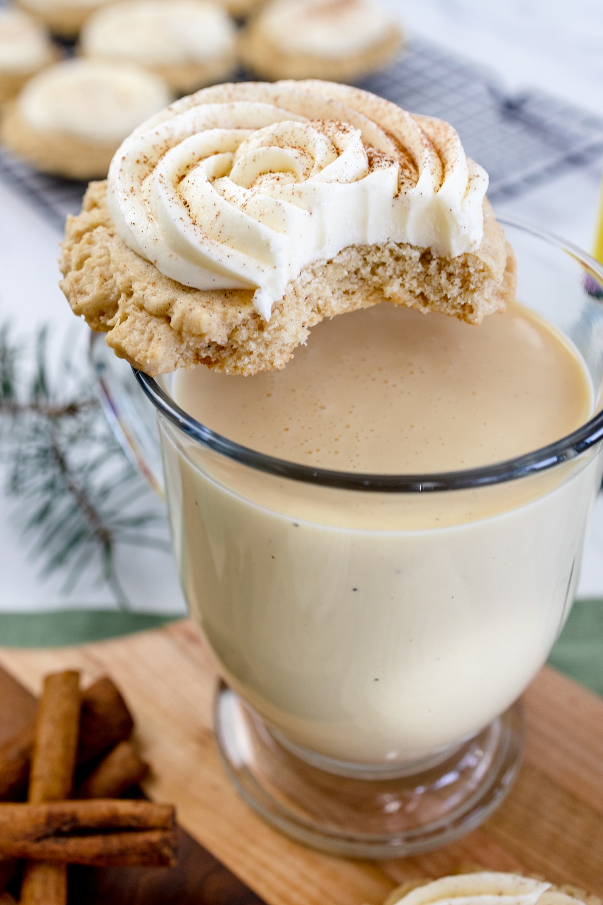 Close up of a glass of eggnog with an eggnog cookie with frosting on top with a bite taken out of it.