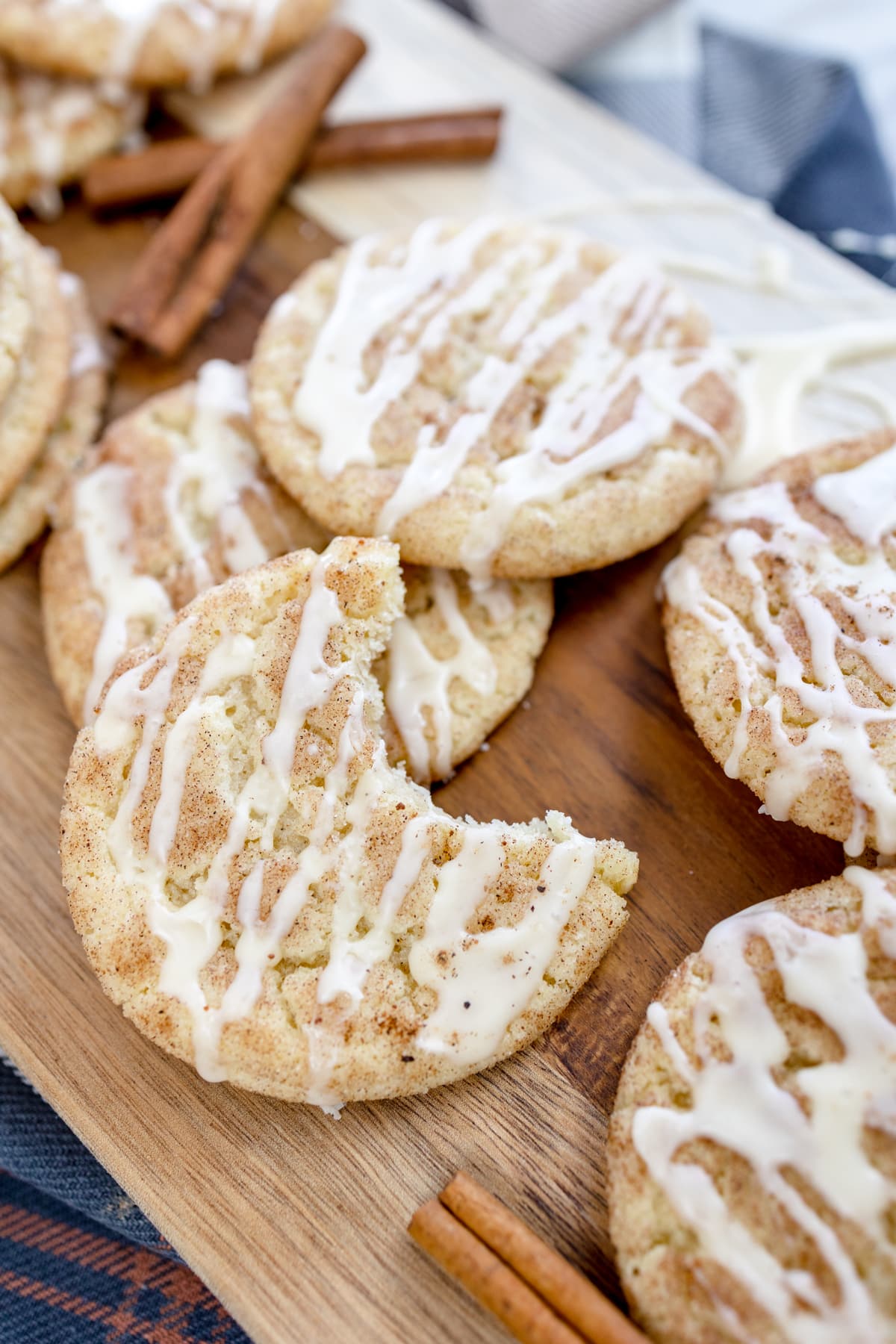 Close up of eggnog snickerdoodle cookies with glaze in a pile on a wooden chopping board.