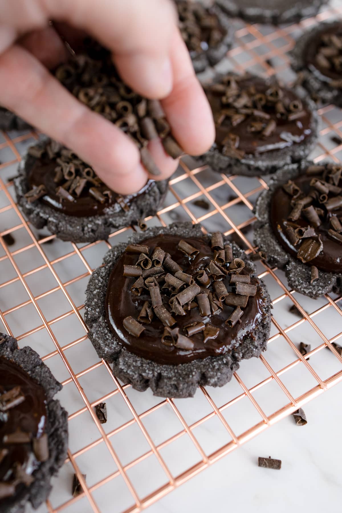 Close up of chocolate curls being sprinkled on top of chocolate ganache on a chocolate sugar cookie.