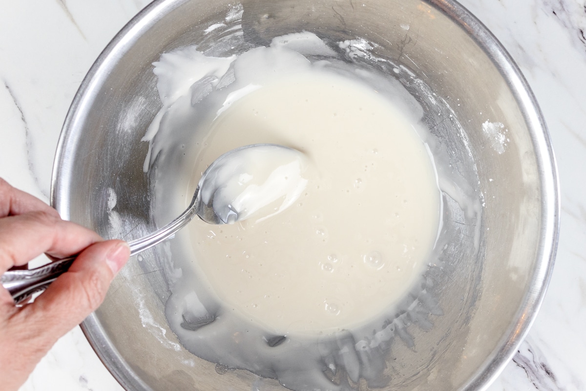 Top view of icing being stirred in a metal bowl with a spoon.