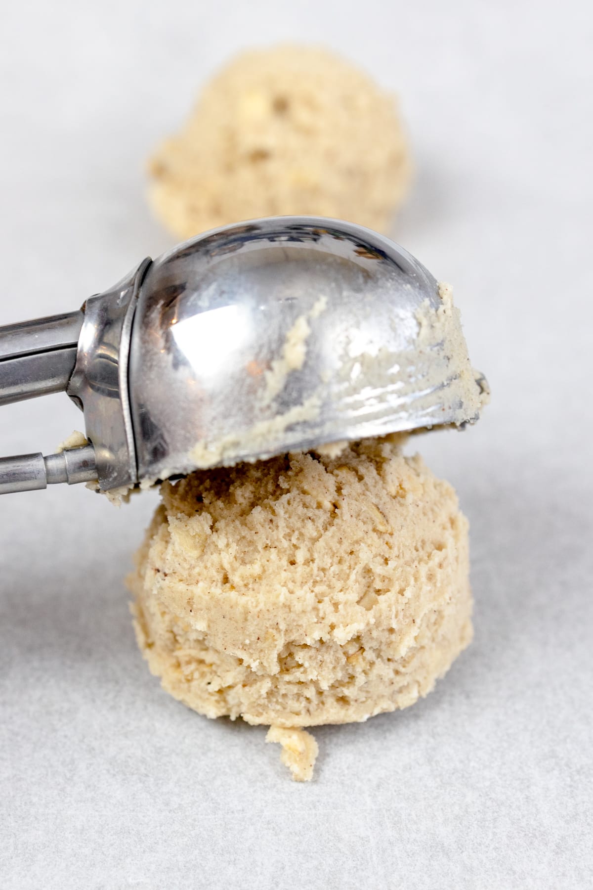 Close up of cookie dough balls being put onto a tray with a cookie scoop.