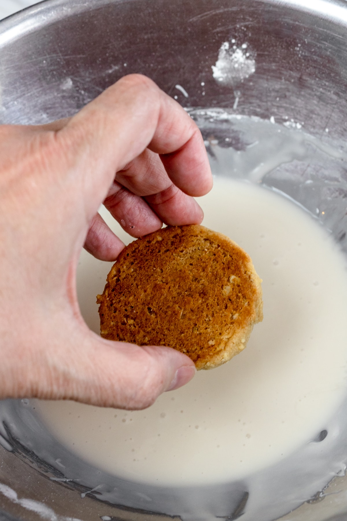 Top view of an oatmeal cookie being dunked into a bowl of icing to get icing on the top of the cookie.s.