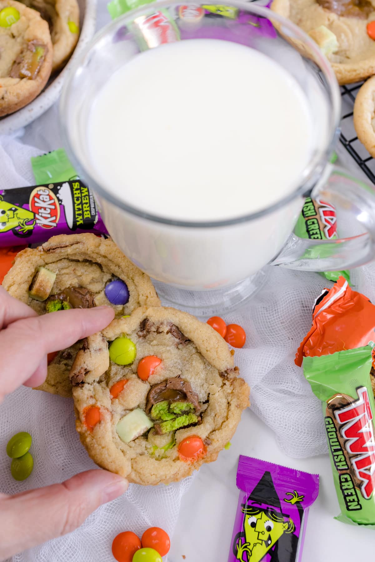 Candy bar cookie being held in front of a tall glass of milk.