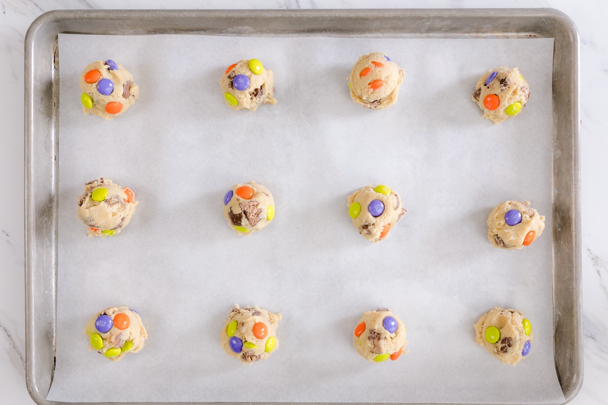 Top view of dough balls of candy cookies on a baking tray on parchment paper. 