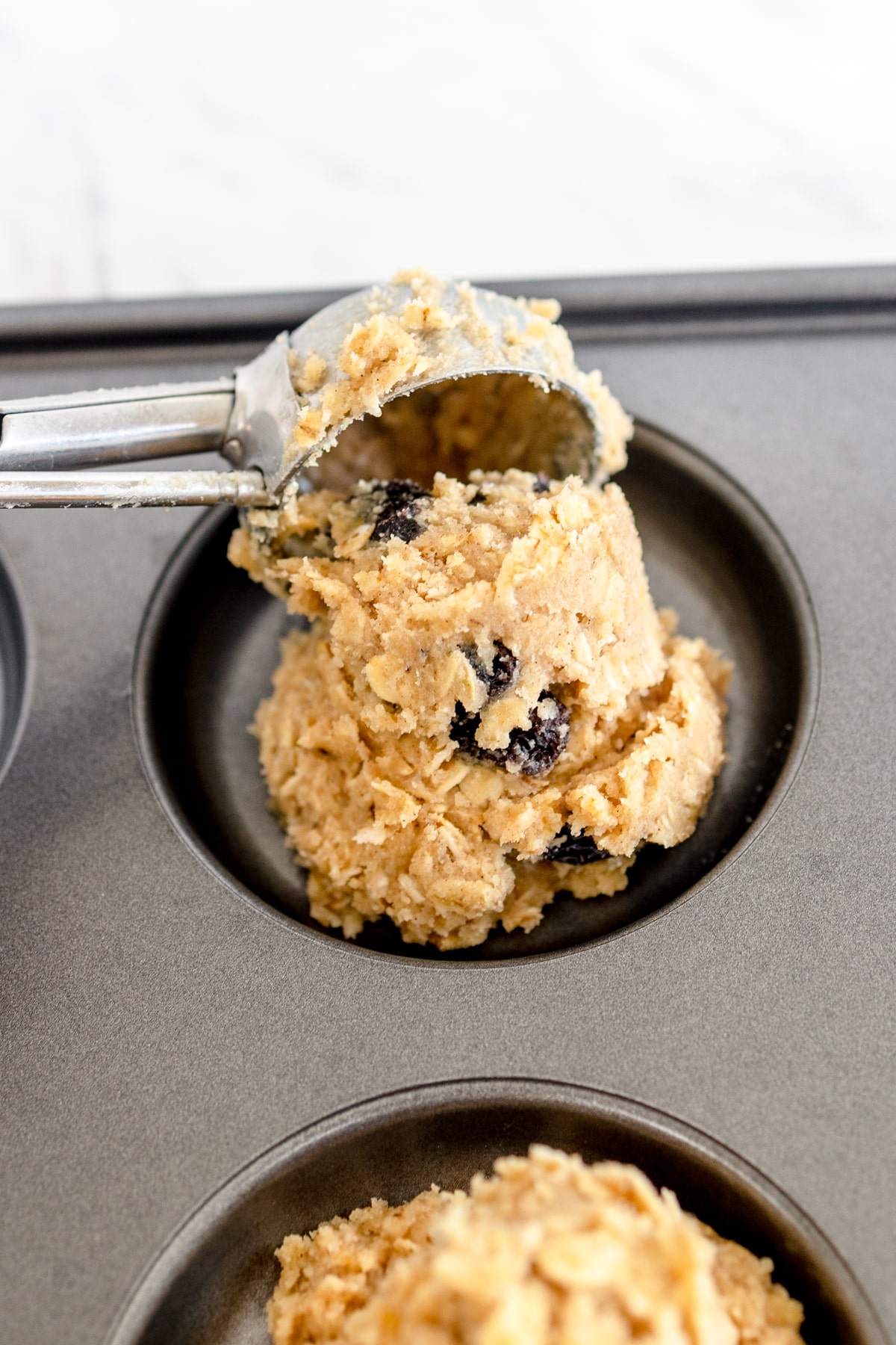 Close up of oatmeal cookie dough being scooped into a cookie baking pan. 