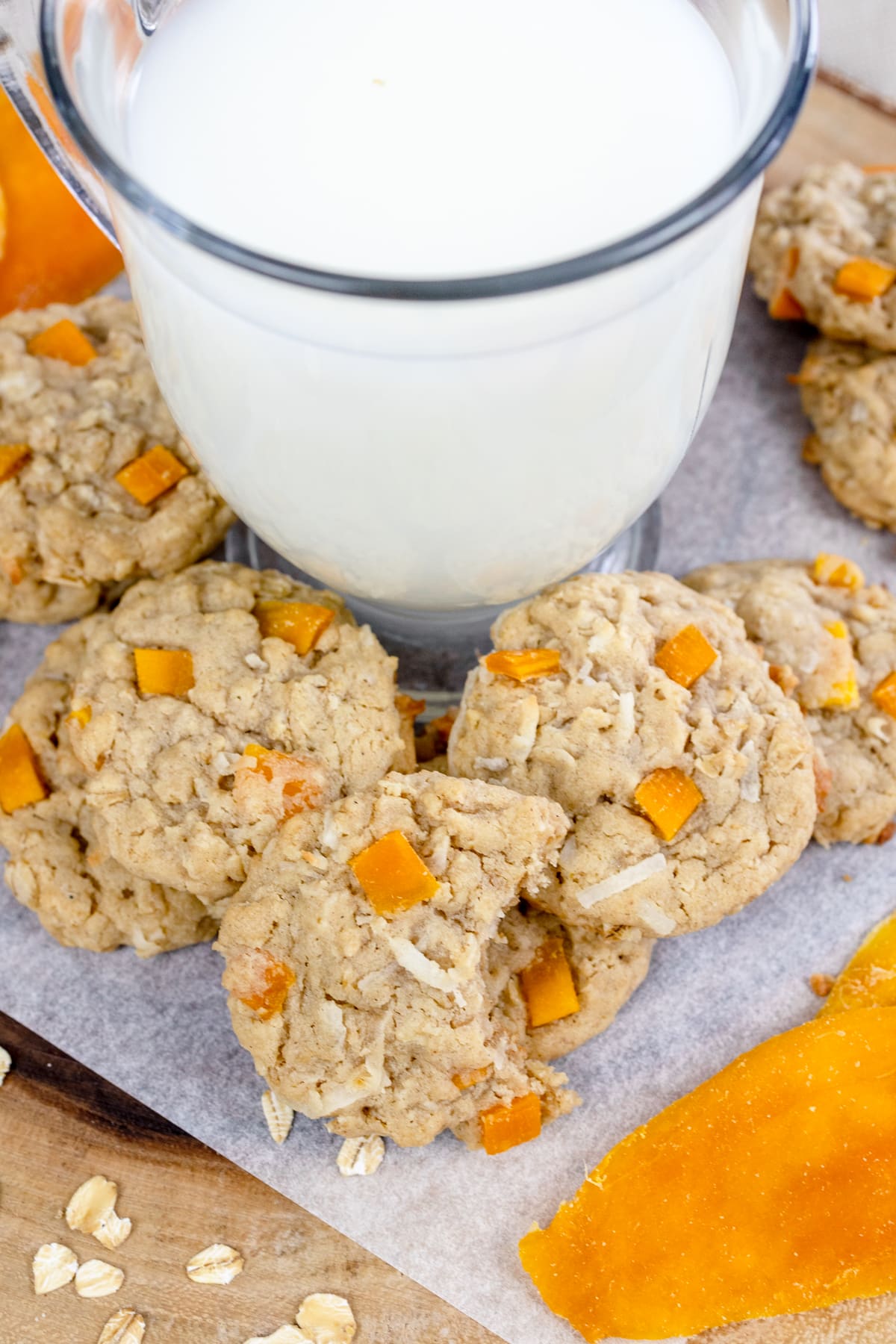 Large glass of milk surrounded by oatmeal mango cookies.