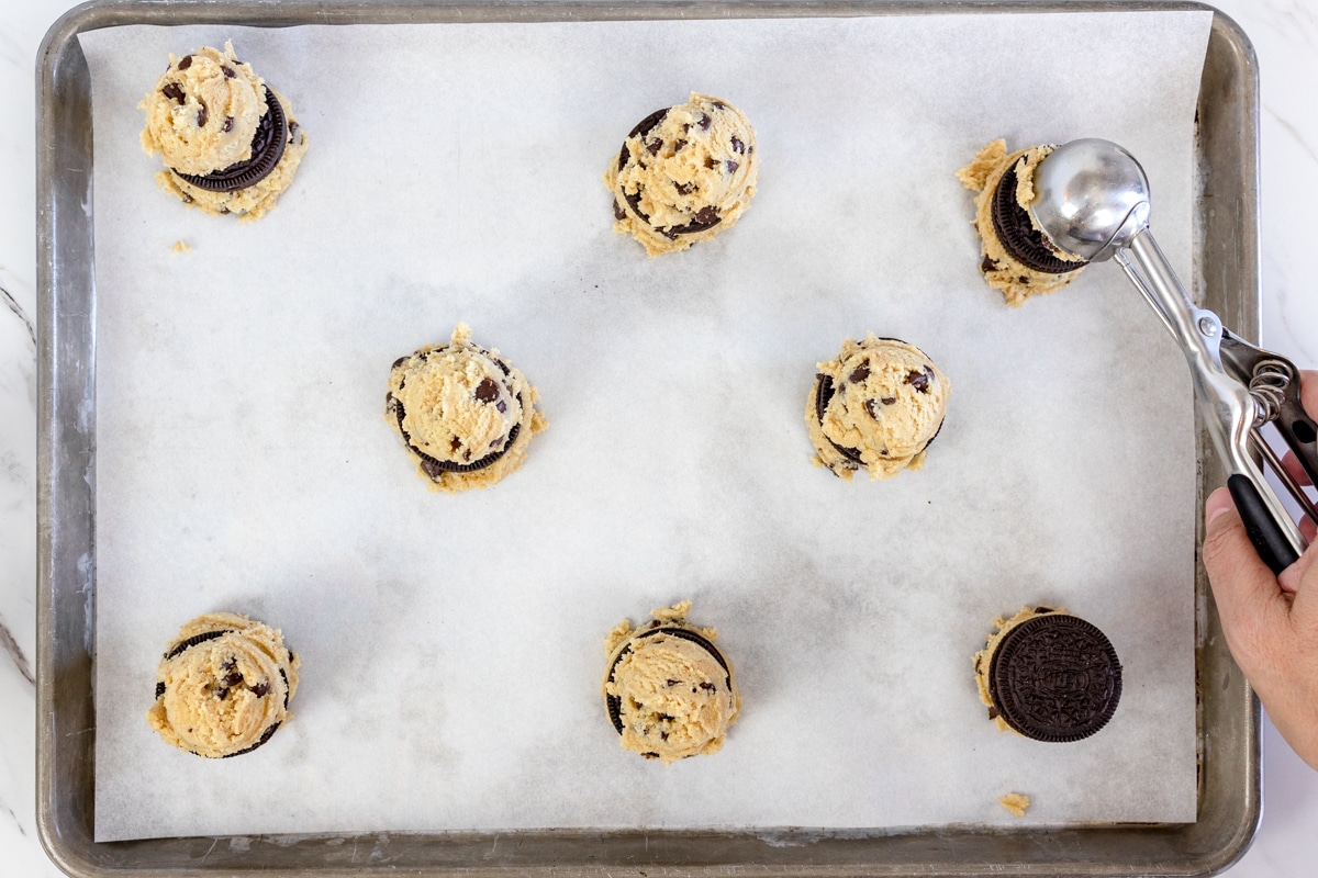 Top view of baking tray with chocolate chip cookie dough balls with an Oreo on each one, and another cookie dough ball on top of the Oreos. 