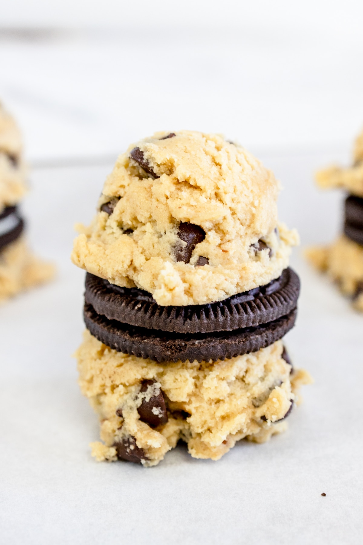 Close up of an Oreo being sandwiched between two cookie dough balls. 