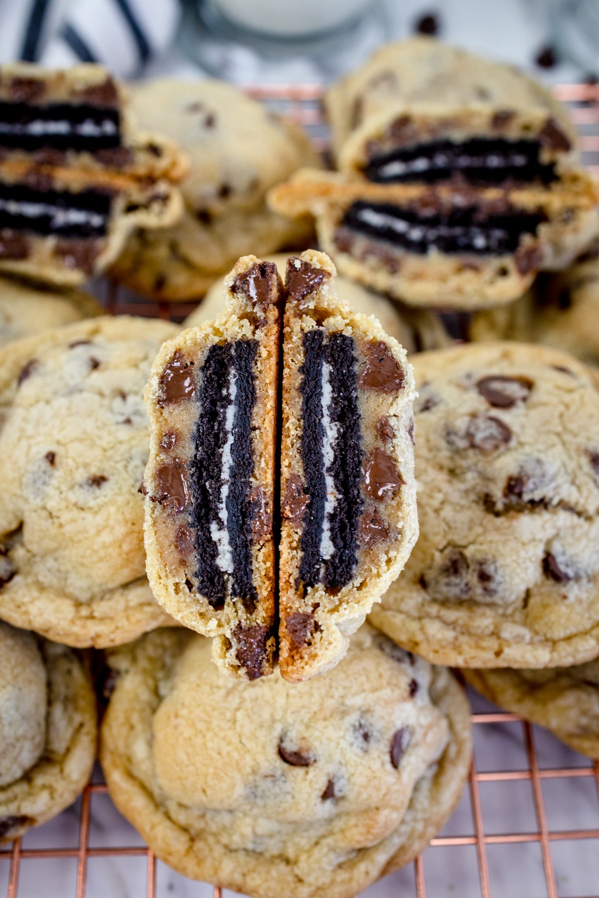 Close up of an Oreo stuffed chocolate chip cookie cut in half being helf up in front of a pile of other cookies.