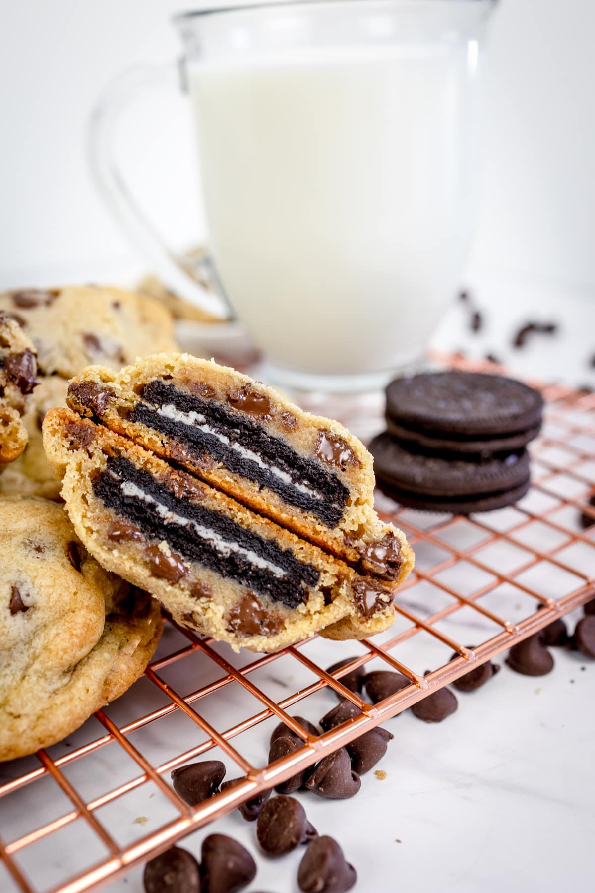 Close up of an Oreo stuffed cookie cut in half in front of a tall glass of milk. 
