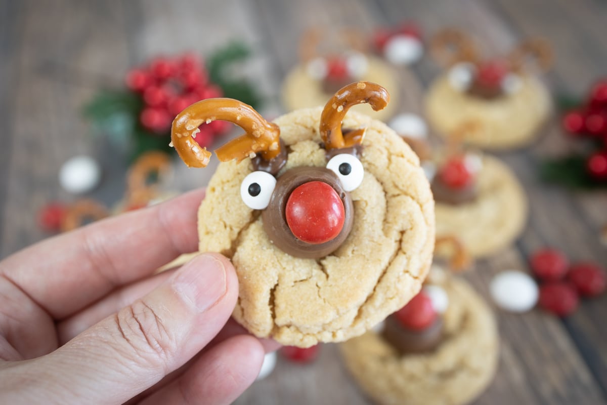 Close up of reindeer cookie being held up with lots of reindeer cookies in the background.