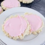 Close up of two sugar cookies with pink frosting on a white plate.