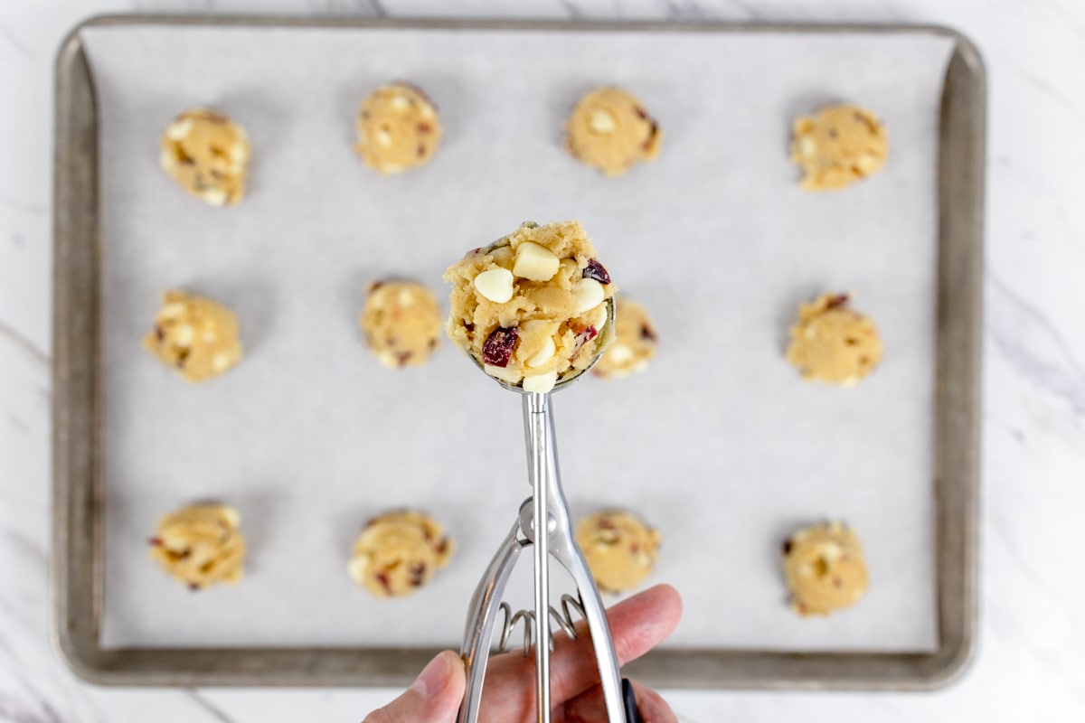 Top viee of baking sheet with cookie dough balls being scooped onto it, evenly spaced out.