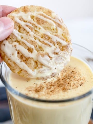 Close up of an eggnog snickerdoodle cookie being dunked into a glass of eggnog.
