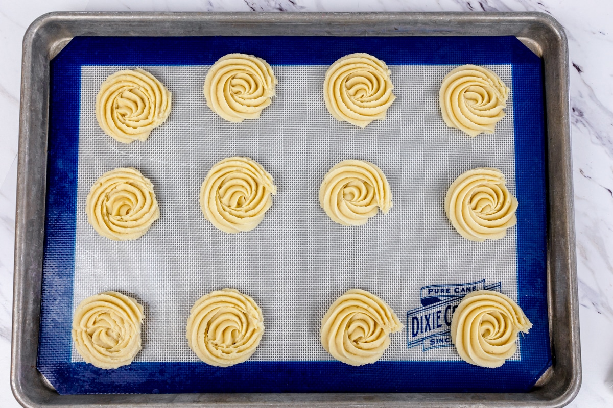 Top view of butter cookies in rosette shapes lined up on a baking tray.