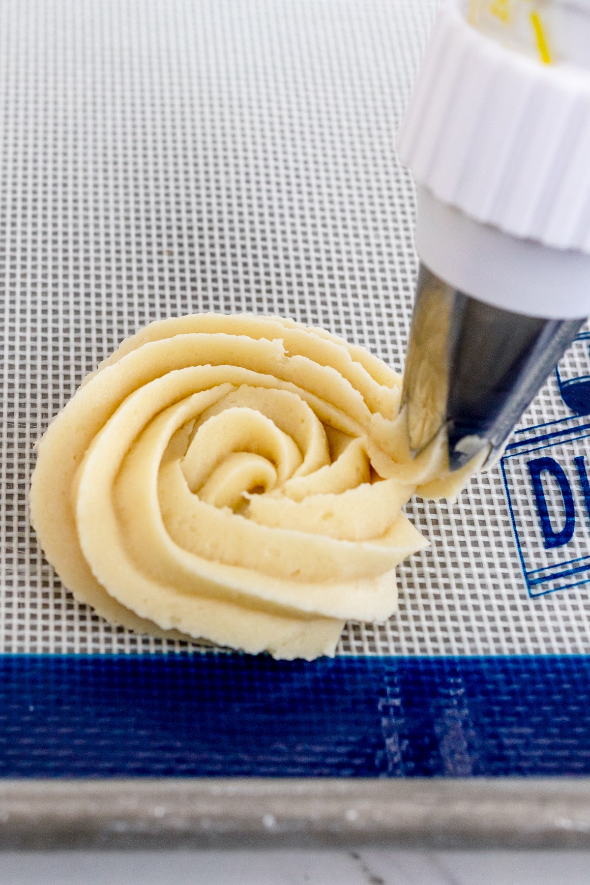 Close up of butter cookie dough being piped into a rosette shape.