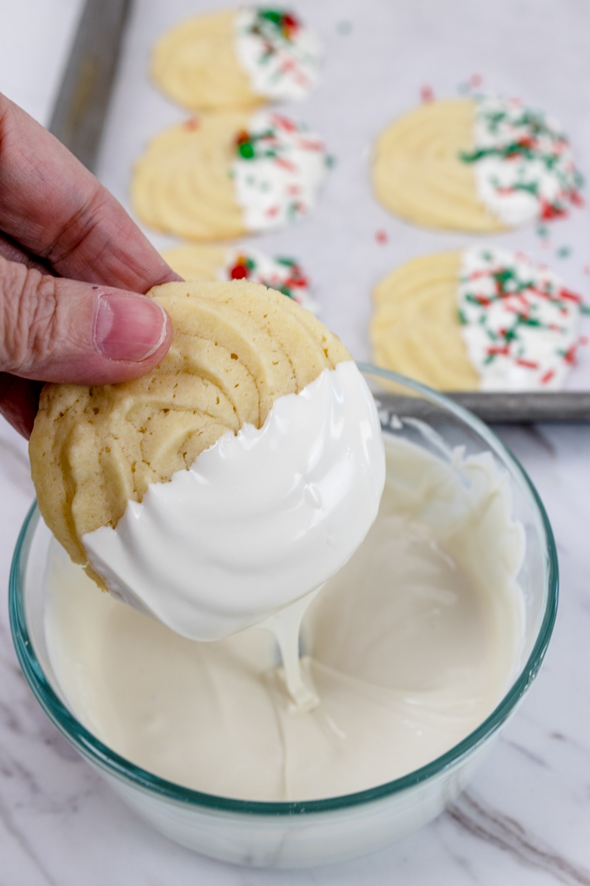 A butter cookie being dipped into melted white chocolate.