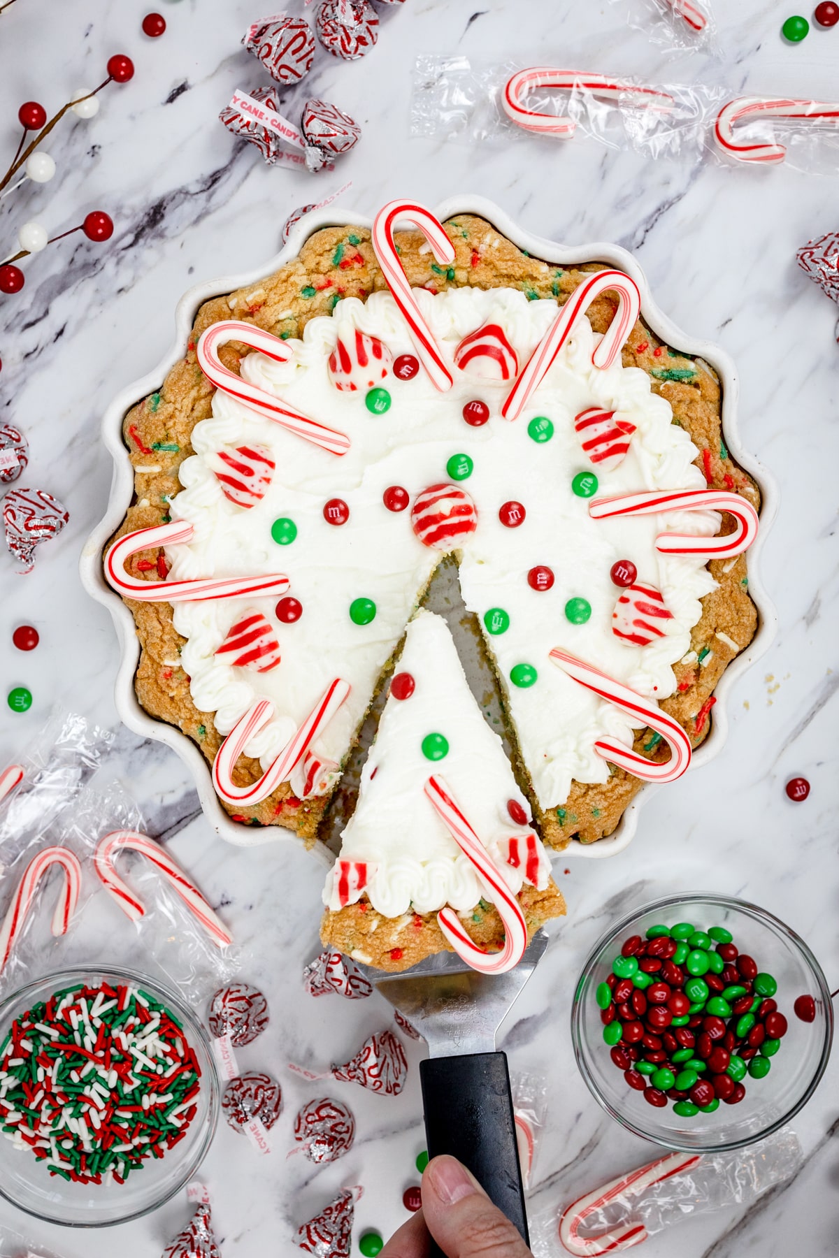 Top view of a Christmas sugar cookie pie with frosting and christmas candies on it with a slice cut out.