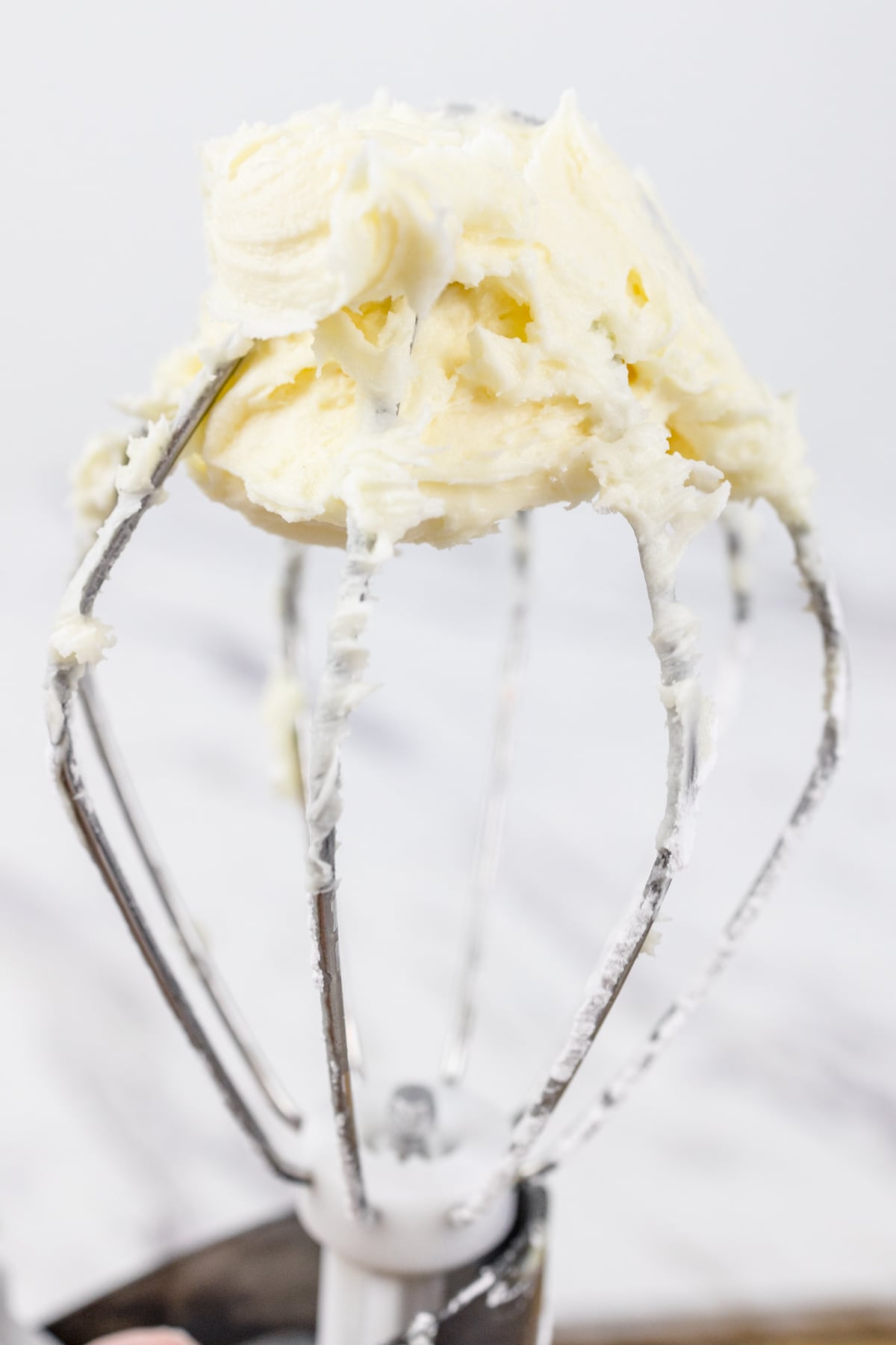 Close up of a whisk attachment with buttercream frosting on the tip.