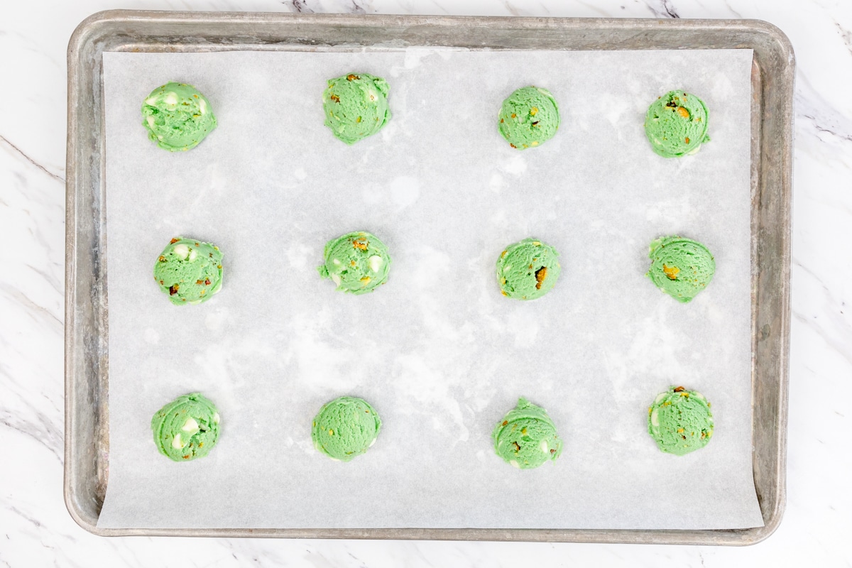 Top view of pistachio cookies dough balls lined up on a baking tray with parchment paper on it