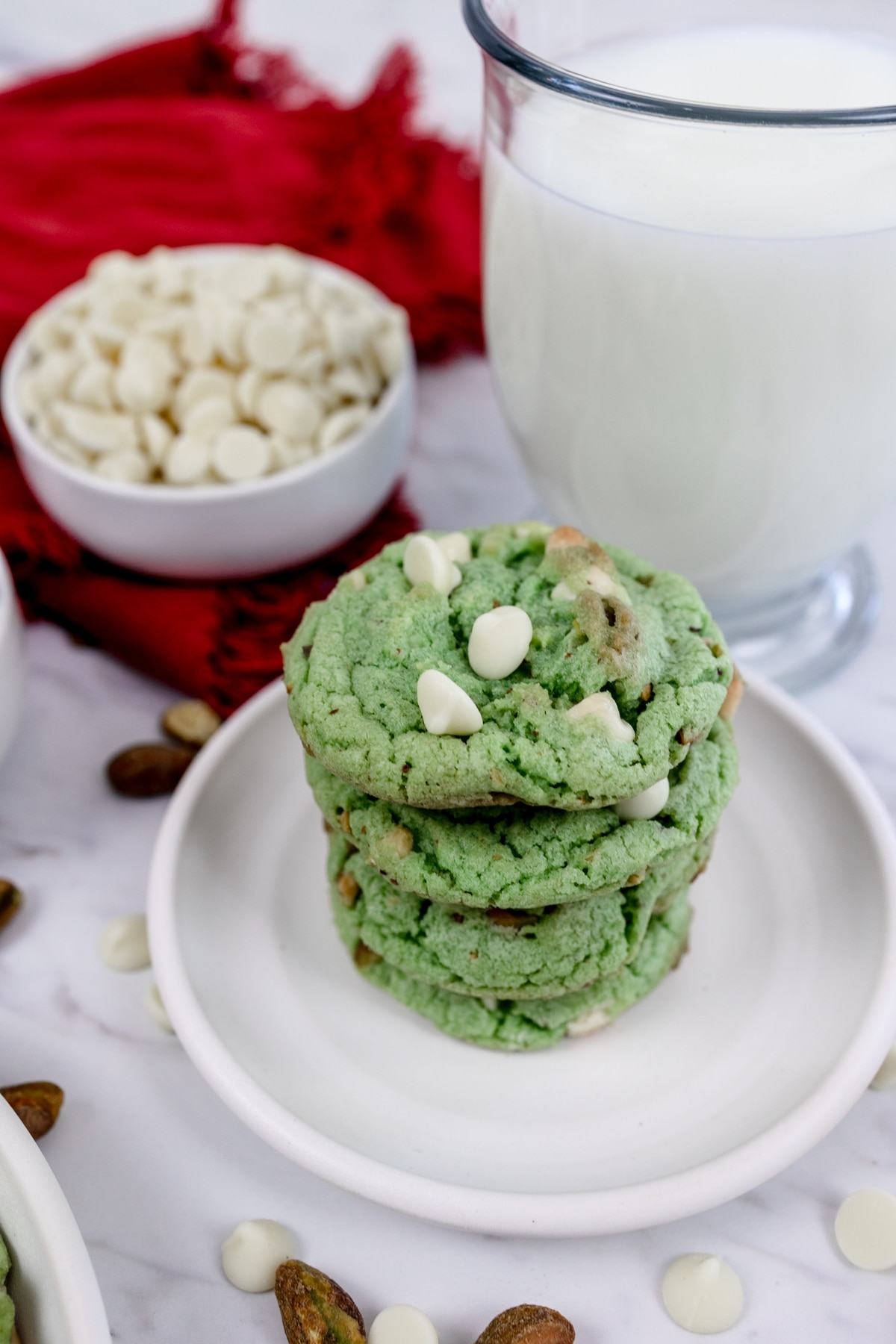 A stack of pistachio pudding cookies on a white plate with a glass of milk behind it.