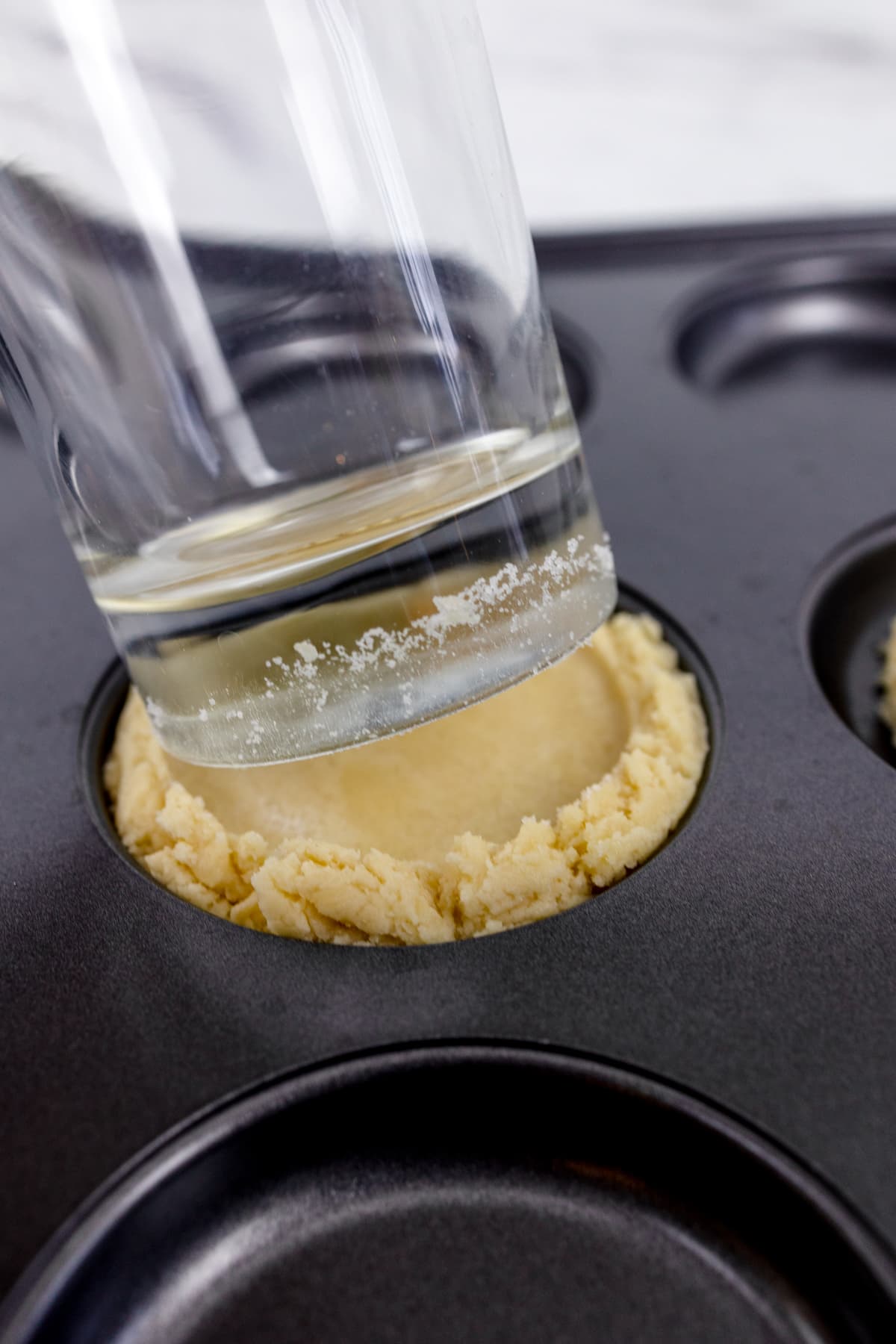 Close up of cookie dough being flattened by a glass. 