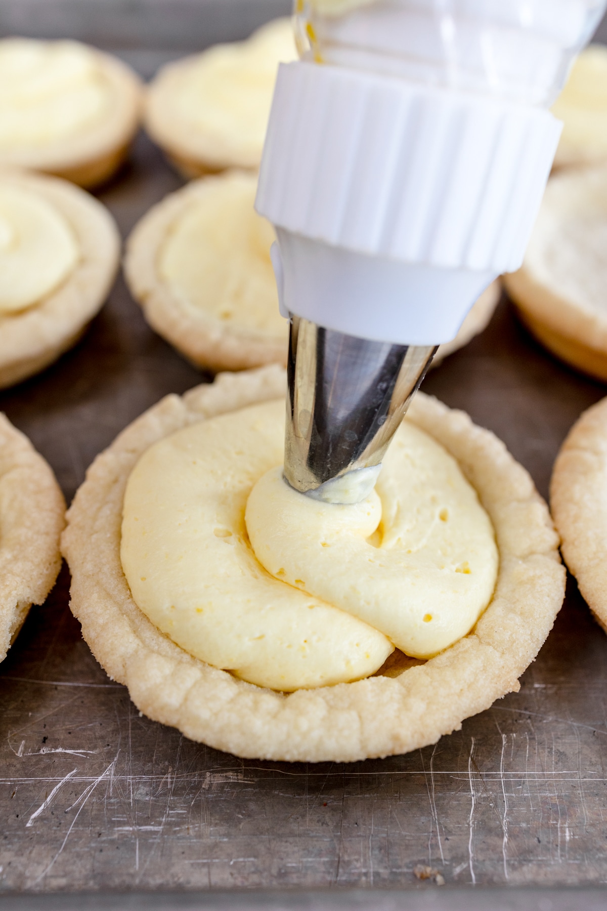 Close up of a cookie being topped with a cream filling using a pastry bag. 
