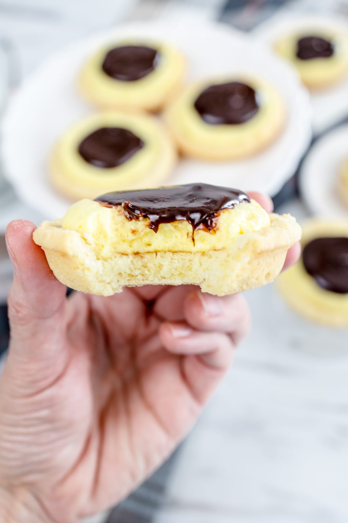 Boston cream pie cookie with a bite taken out of it being held in mid air by a hand.