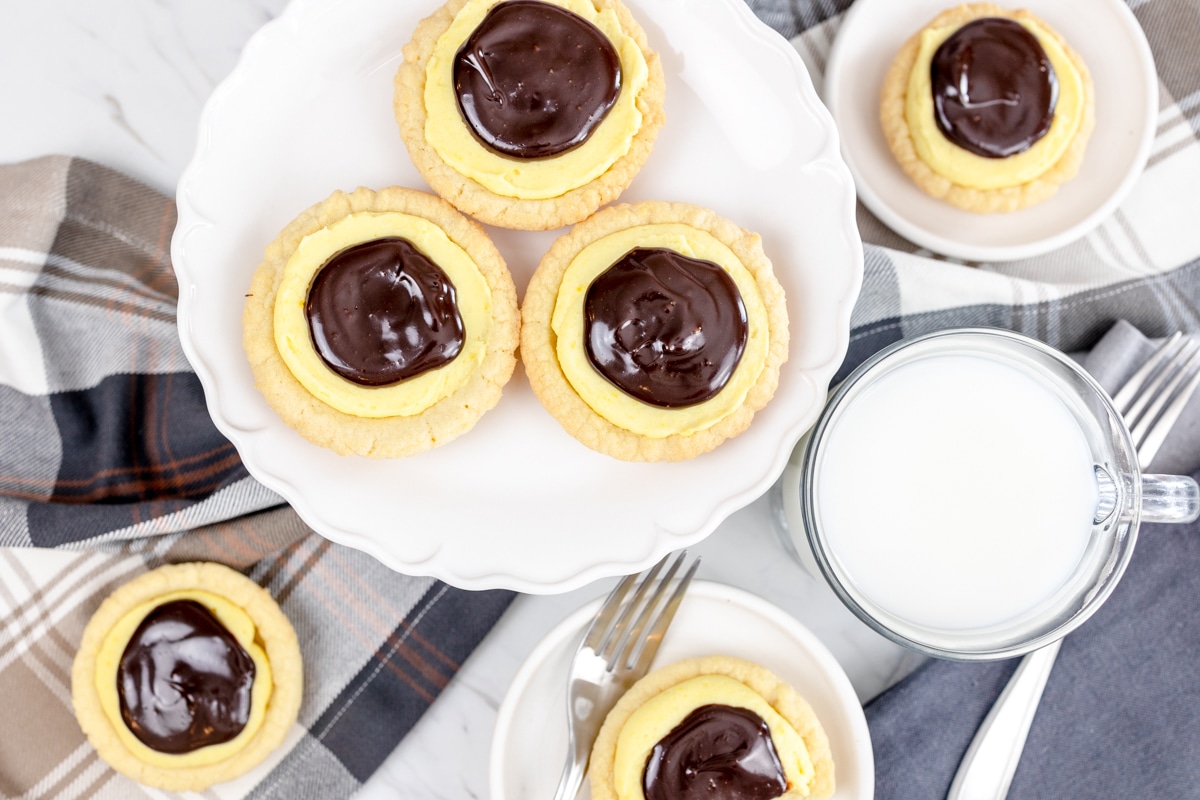 Top view of Boston cream pie cookies on a white plate, with other cookies on the table around it. 