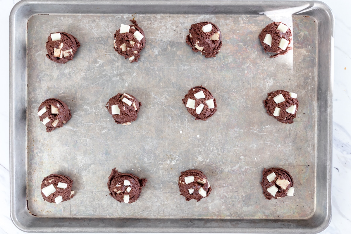 Top view of peppermint bark cookie dough balls on a baking tray with peppermint bark pieces on top. 