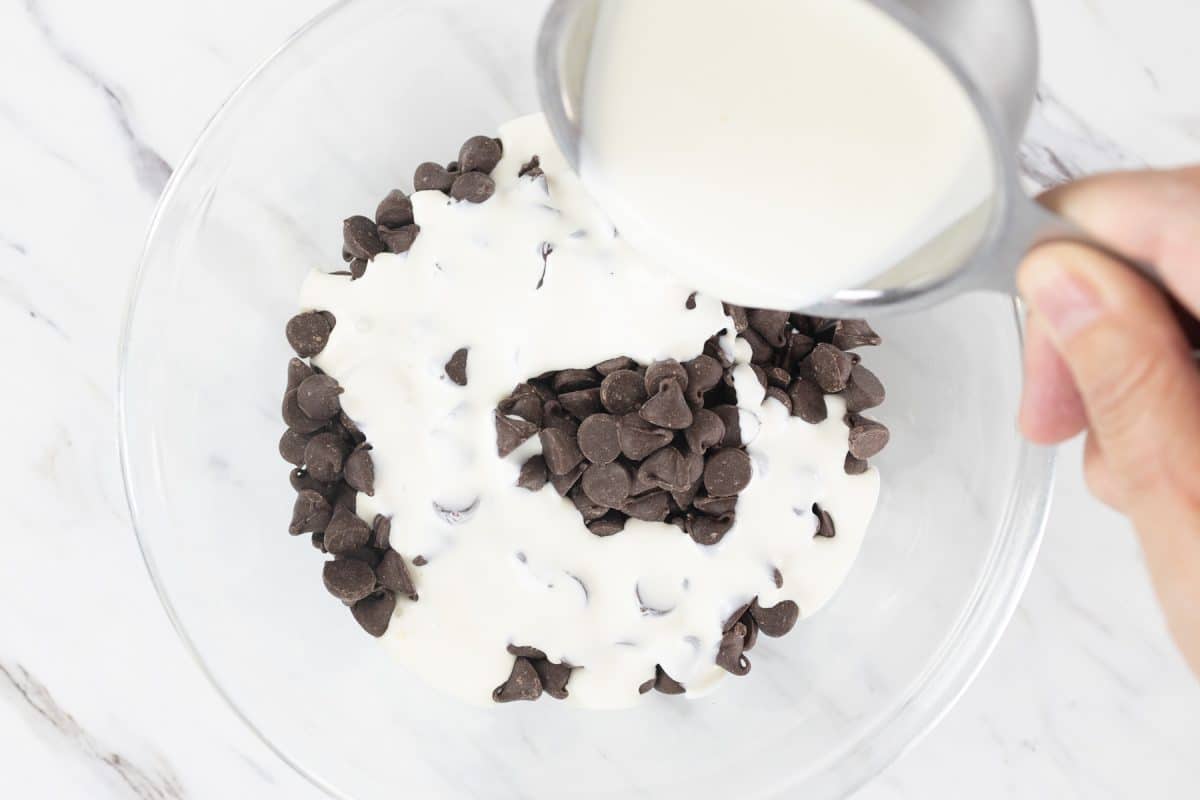 Top view of a glass bowl with chocolate chips in it and cream being poured over the top. 