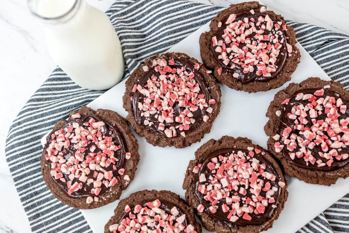 Top view of peppermint chocolate cookies on a white plate next to a glass of milk. 