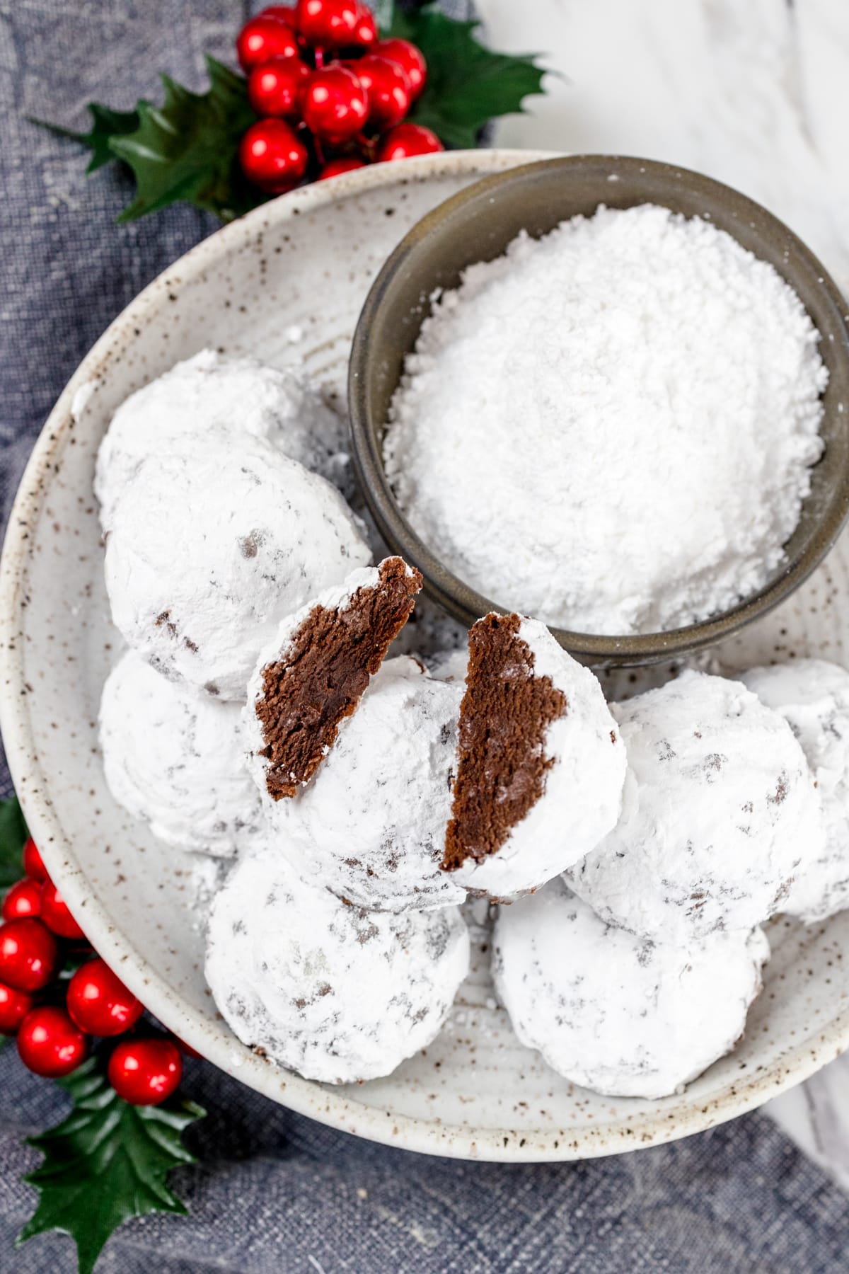 Top view of snowball cookies on a plate next to a small bowl of powdered sugar.