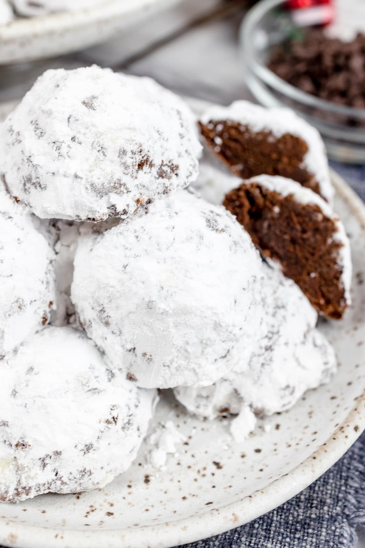 Close up of chocolate snowball cookies stacked on a white plate. 