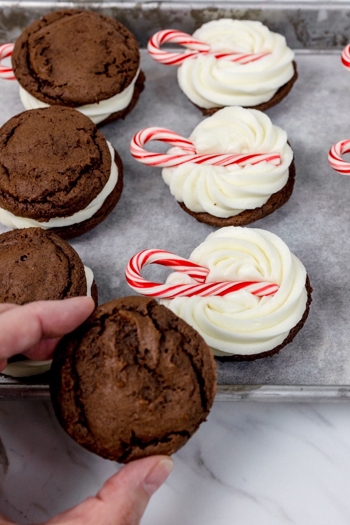Top view of a cookie being placed on top of a cookie with frosting and a candy cane to make a cookie sandwich. 