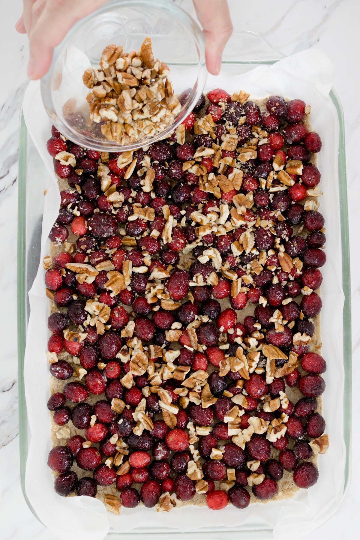 Top view of a baking dish with chopped nuts being added on top of a layer of cranberries. 