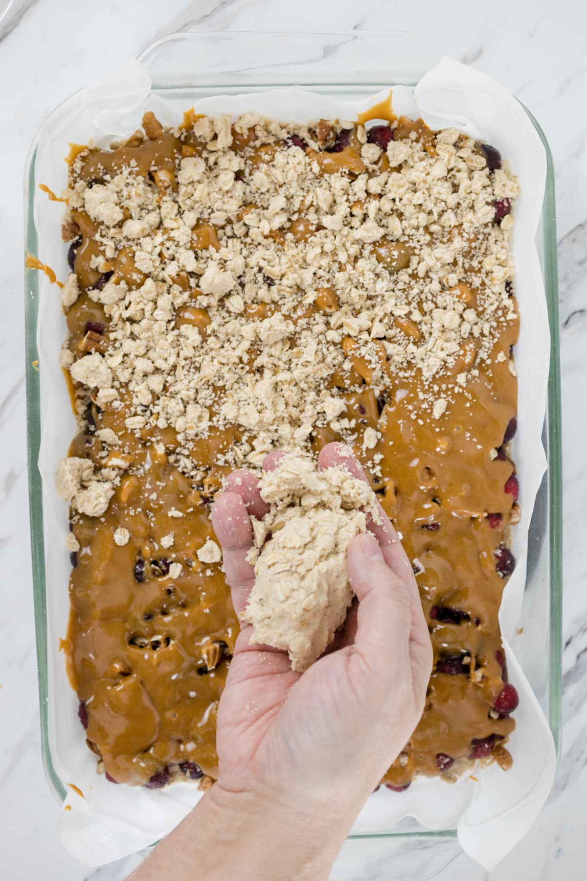 Top view of a baking dish with oats being sprinkled onto a caramel layer. 
