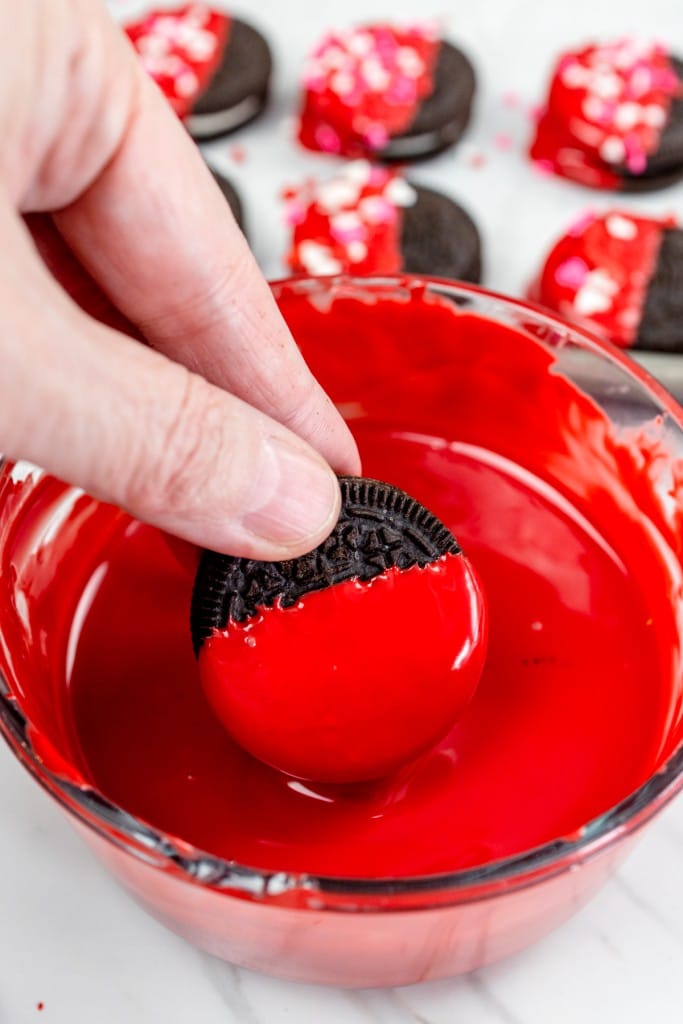 Close up of an Oreo cookie being dipped into a bowl of red icing.