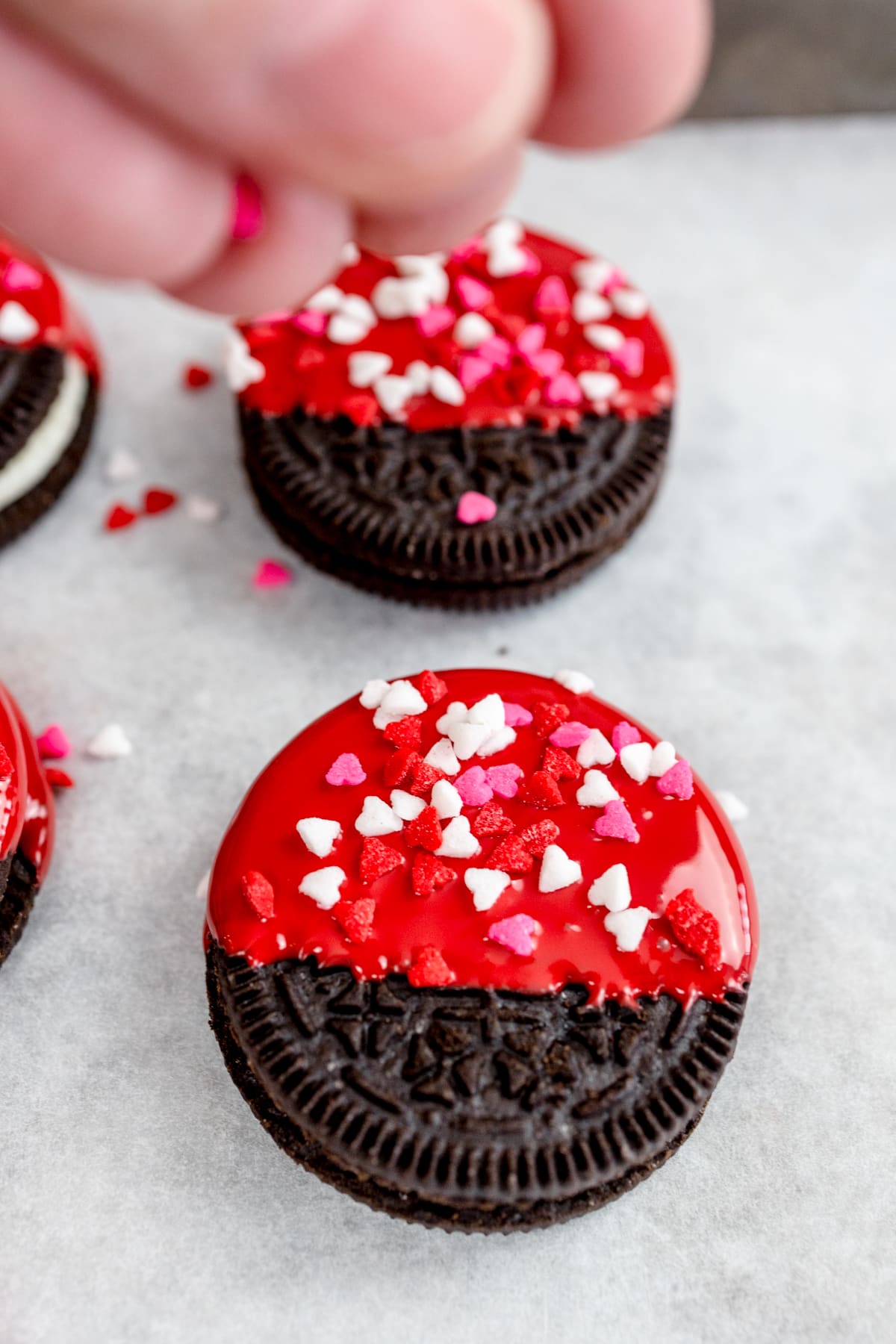 Top view of Oreo cookies half covered with red icing, with heart-shaped sprinkles on the icing. 