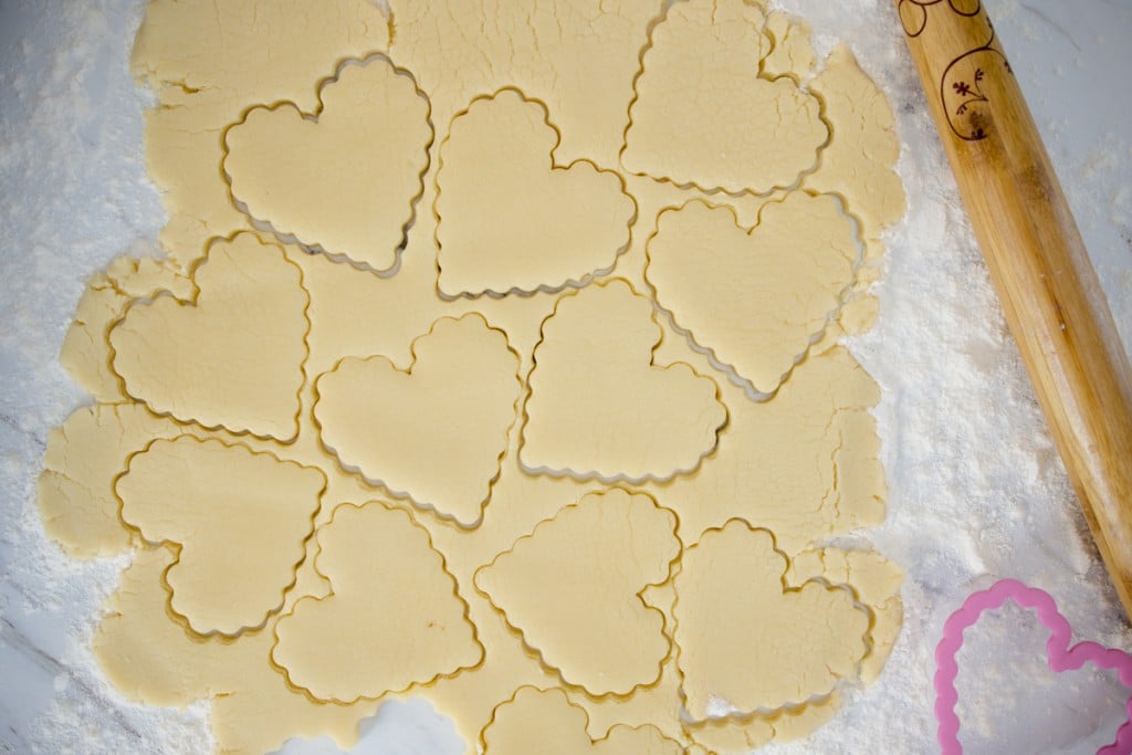 Top view of sugar cookie dough rolled out on to a worktop with heart shapes cut into it. 