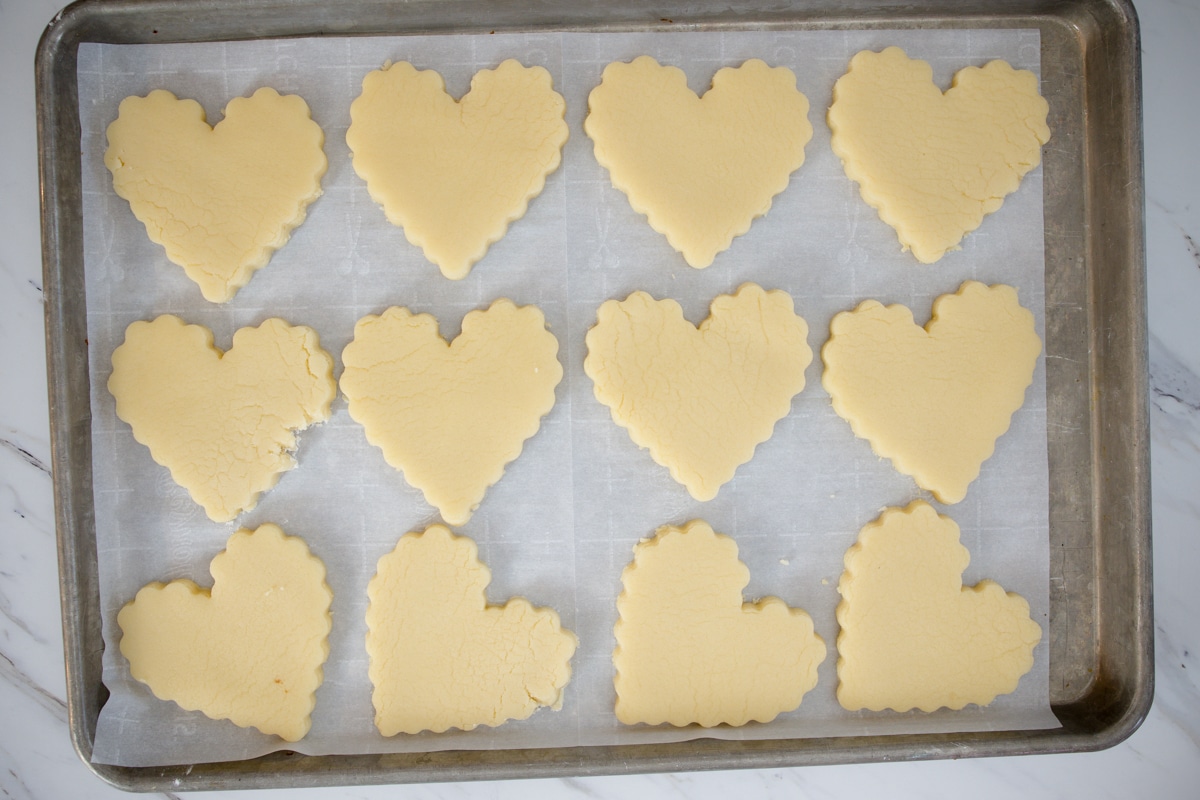 top view of heart-shaped cookie dough cookies on a baking tray. 