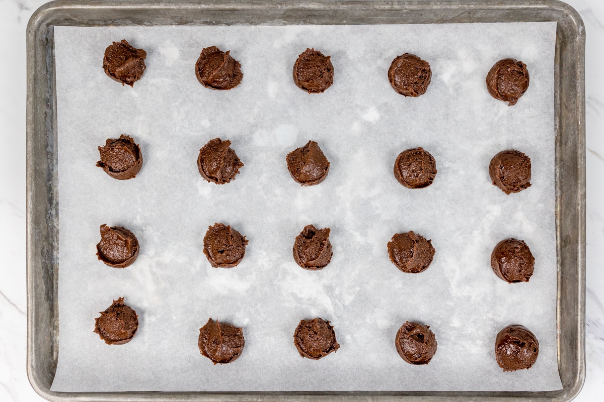 Top view of a baking tray with chocolate cookie dough balls on it. 