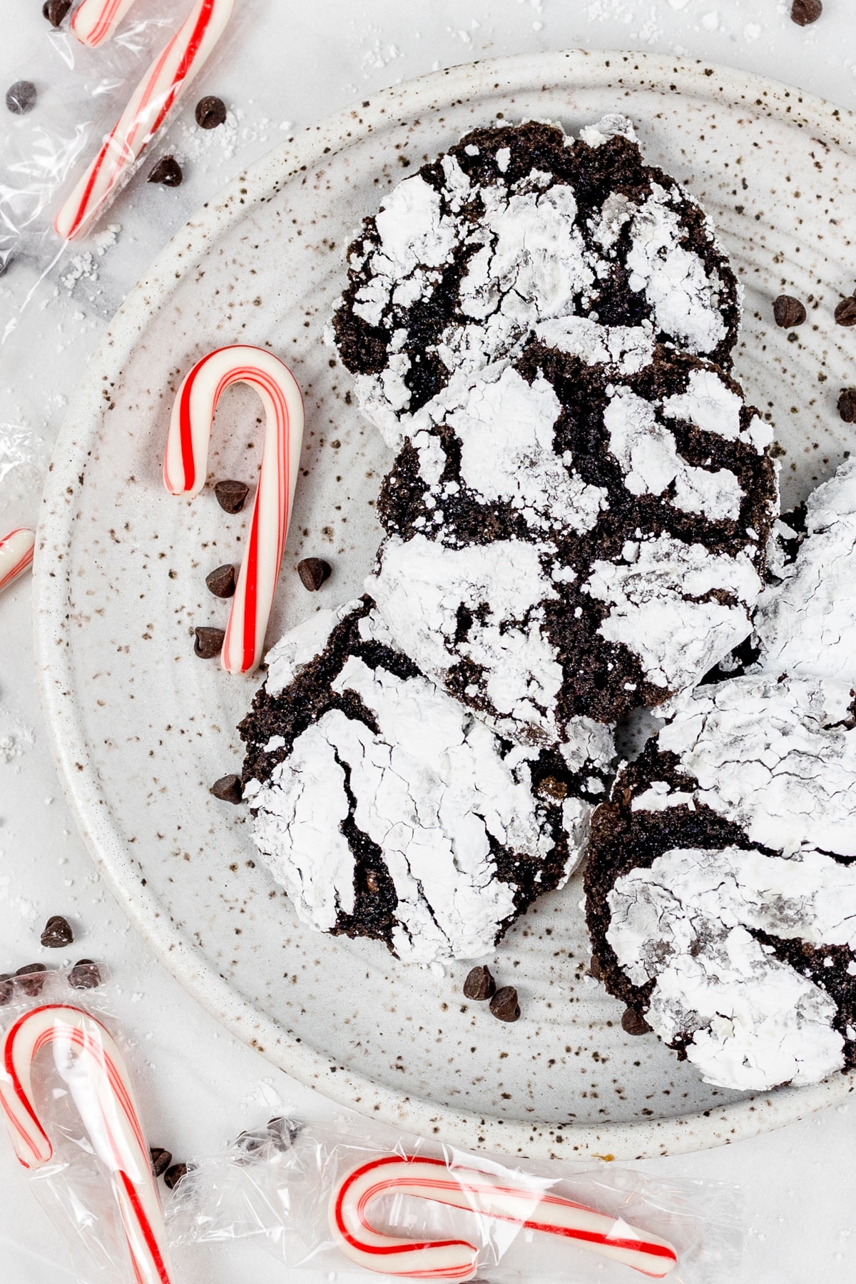 Top view of chocolate peppermint crinkle cookies on a white plate with candy canes around it. 