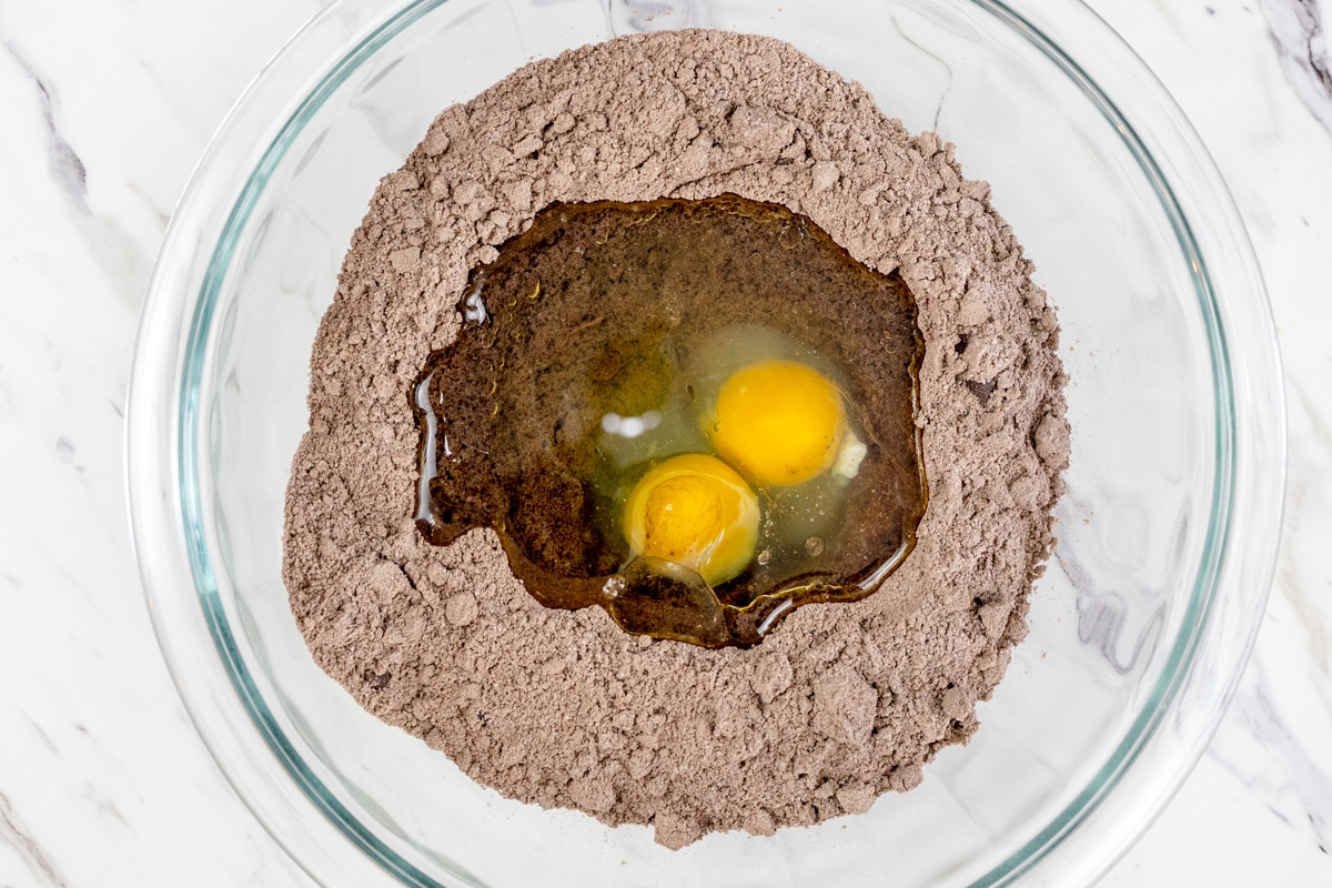 Top view of chocolate loaf mix in a glass mixing bowl with two eggs in the middle. 
