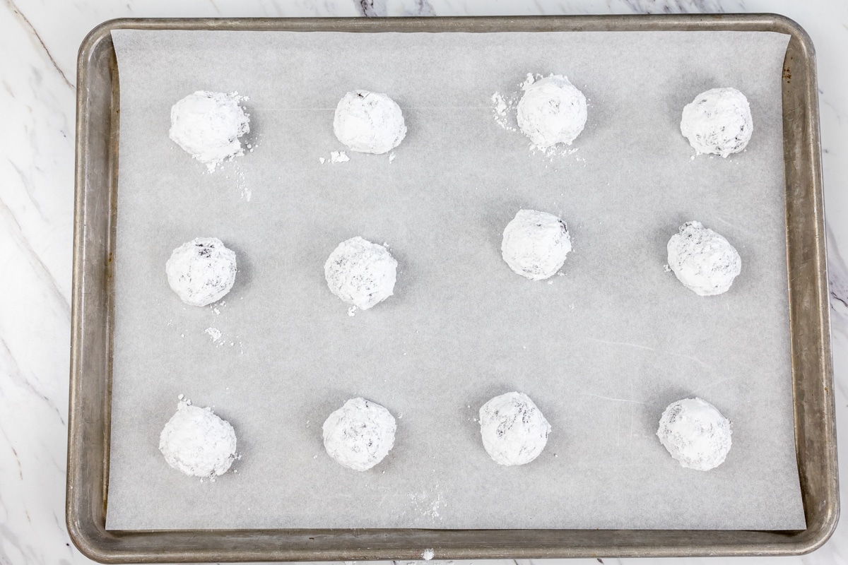 Top view of cookie dough balls covered in powdered sugar on a baking tray. 