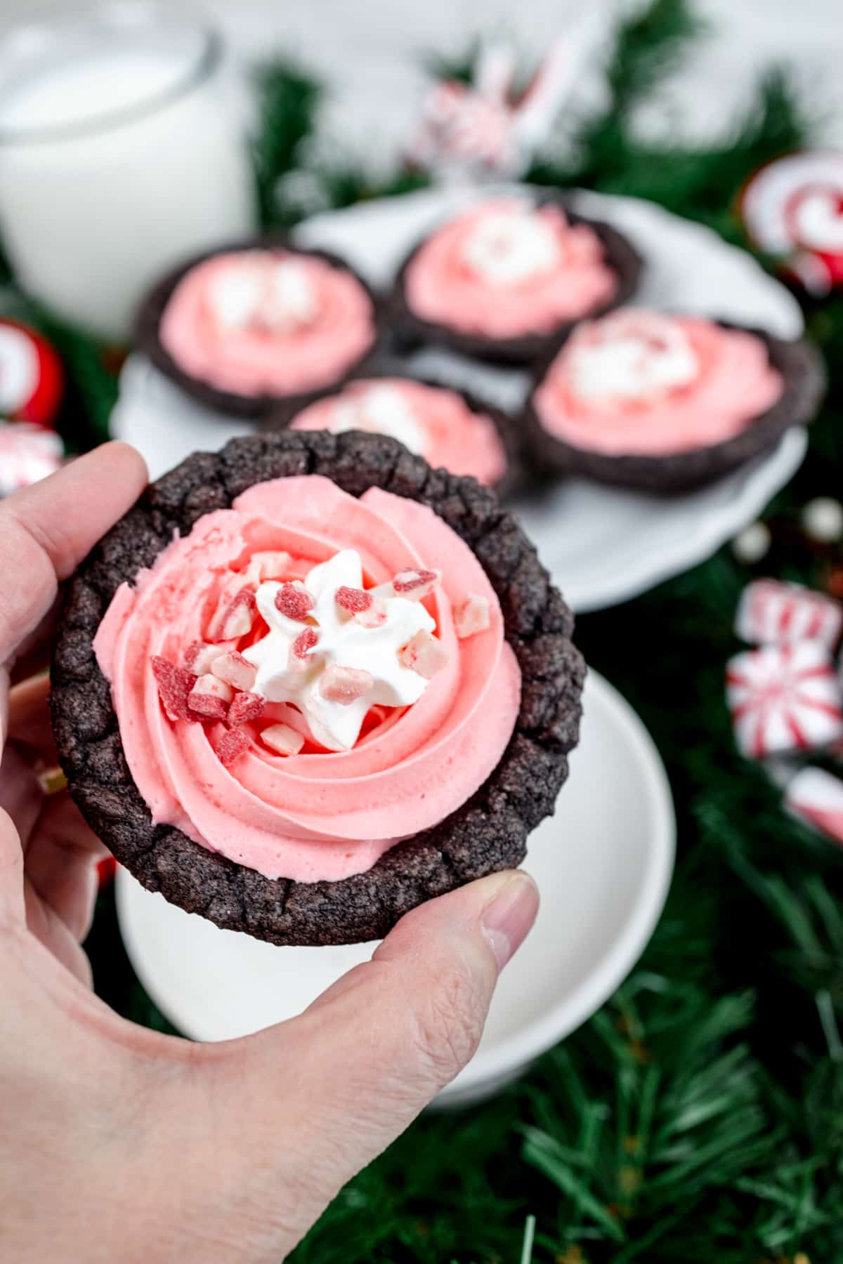 Close-up of a peppermint pie cookie being held in mid-air with other peppermint pie cookies in the background. 