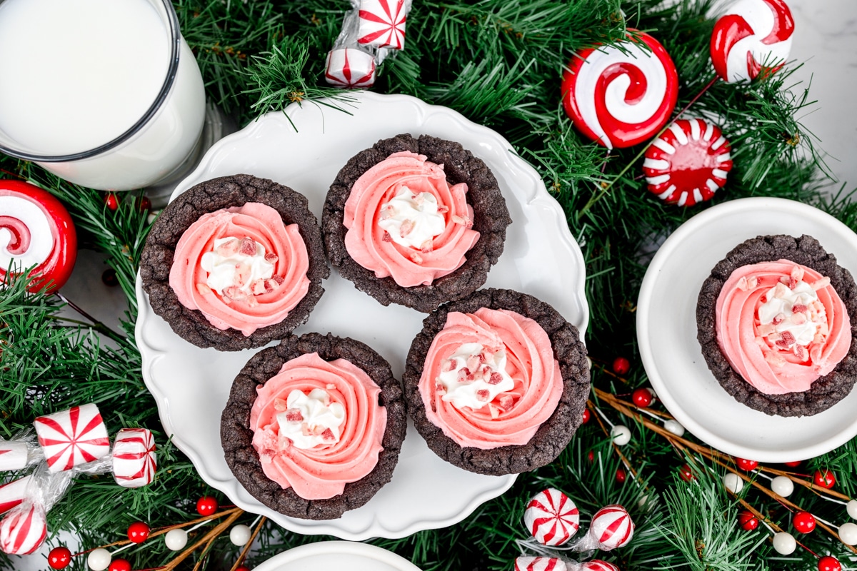 Top view of peppermint pie cookies on a white plate, surrounded by Christmassy candy and other cookies. 