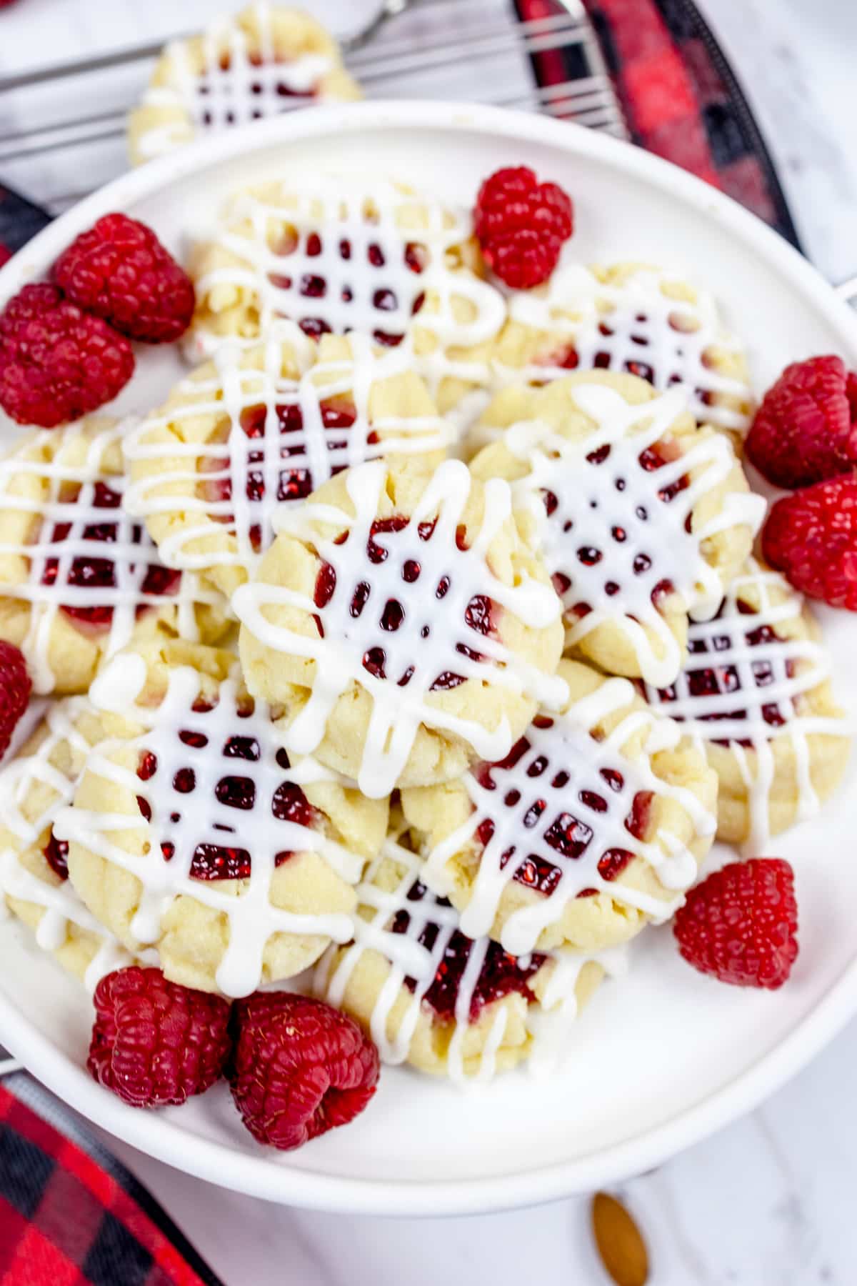 Top view of raspberry thumbprint cookies in a pile on a white plate. 